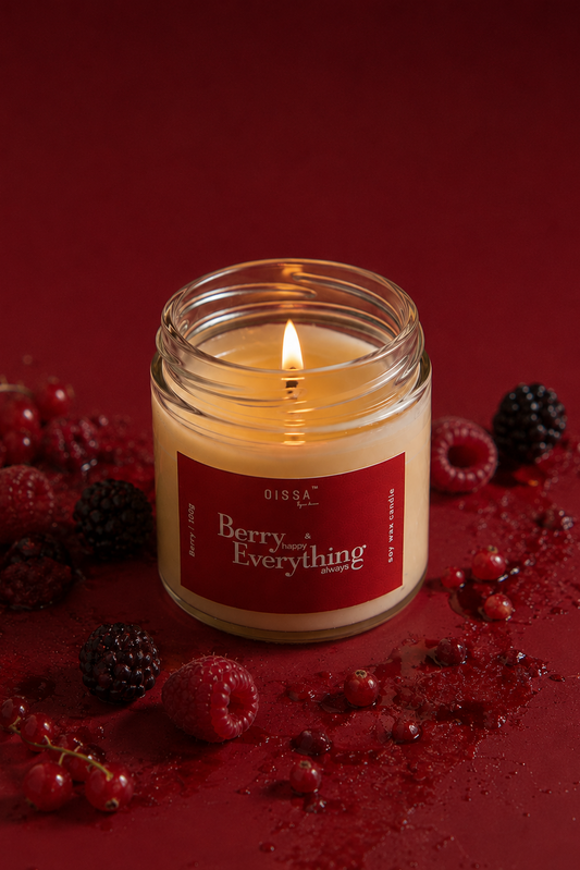 A lit glass jar candle with a red label reading 'Berry Everything' sits on a deep red surface surrounded by fresh berries and berry juice splatter. The brand name 'Qissa by su.i' is visible on the label.
